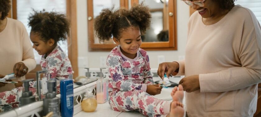 Mother helping two young children brush their teeth