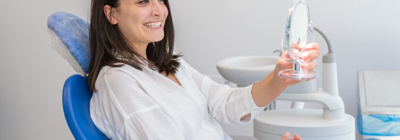 Smiling woman in a dental chair holding a dental tool — Everything You Need to Know About Dental Implants in Fort Collins