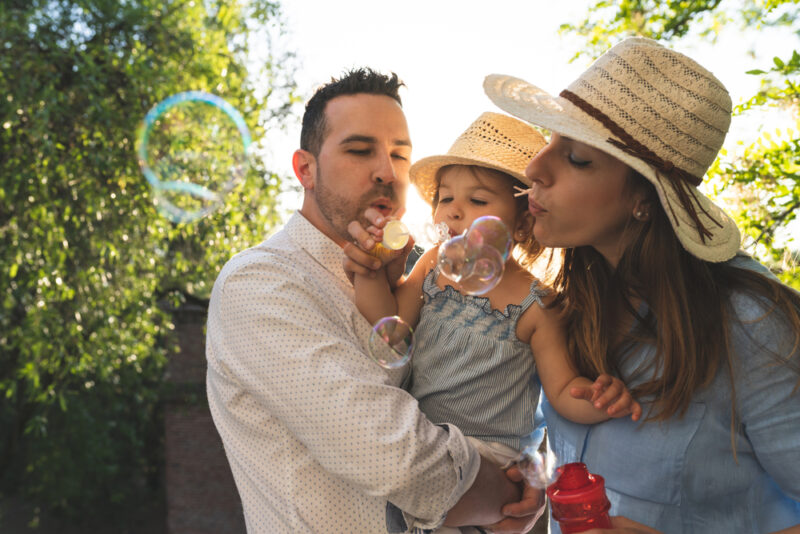 Parents and toddler blowing bubbles together outdoors