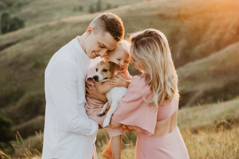 Couple and their child hugging a dog in a field