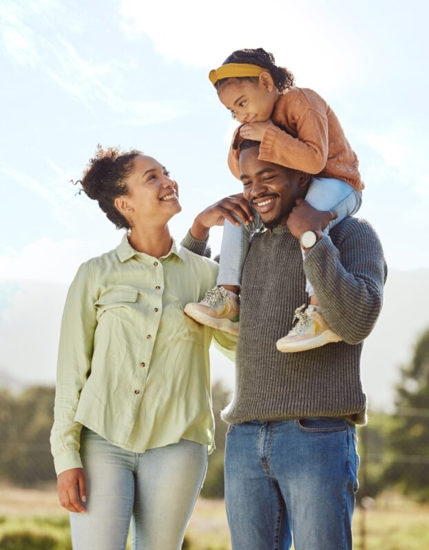 Smiling family walking outdoors with a child on dad's shoulders