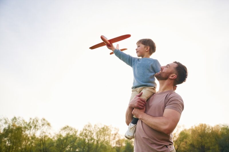Father holding his son up as he flies a toy airplane