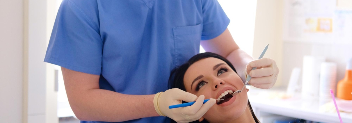 Hygienist cleaning a smiling woman's teeth — Why Regular Teeth Cleanings Are Essential for a Healthy Smile